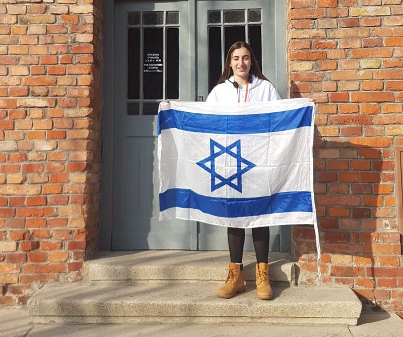 טל אנגל עם דגל ישראל ליד בלוק 27 באושוויץ